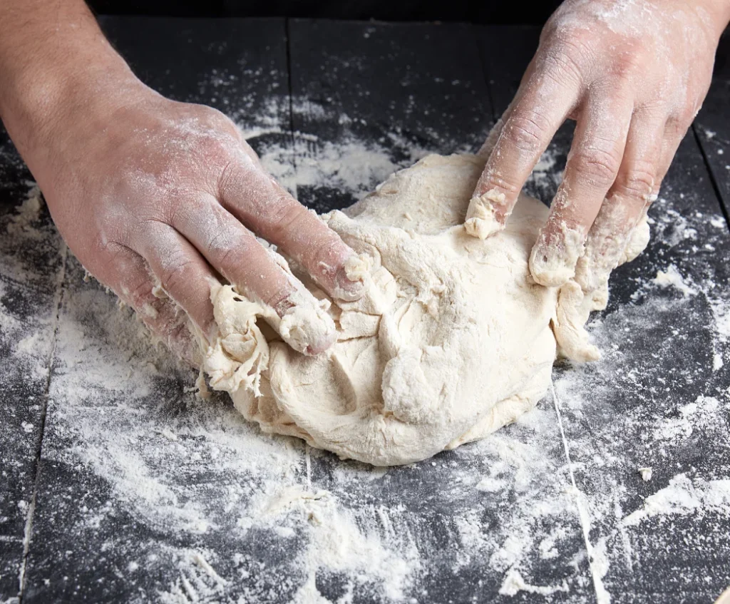 Hands kneading fresh pasta dough on a floured surface — preparation for handmade pasta in Singapore.
