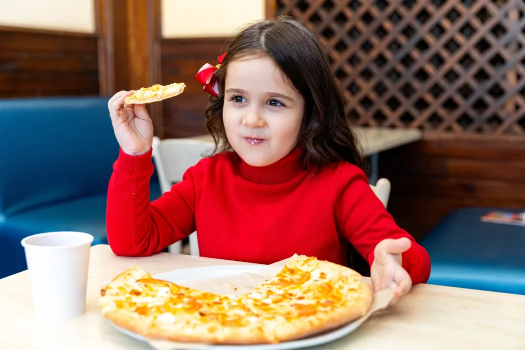 A young girl enjoying a slice of Margherita pizza at a family restaurant in Singapore, highlighting kid-friendly Italian dining and happy mealtime moments.