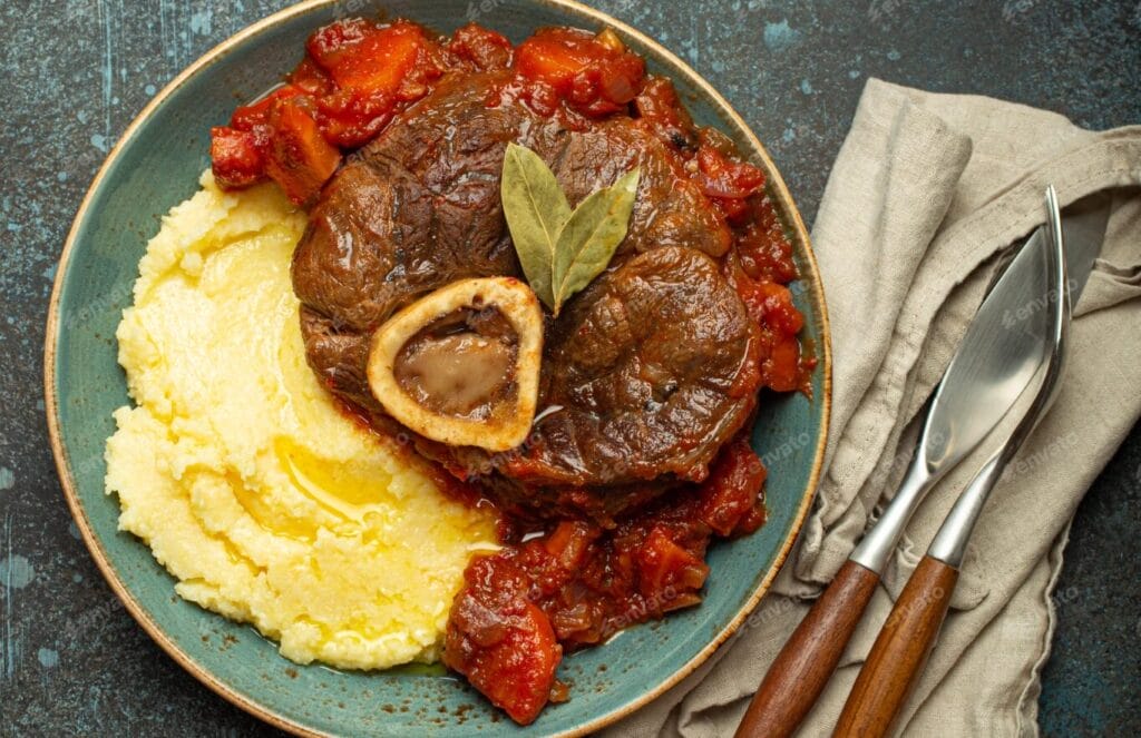 Osso Buco alla Milanese served on green, jade-like dinnerware. A spoon and fork are placed on a napkin at its side
