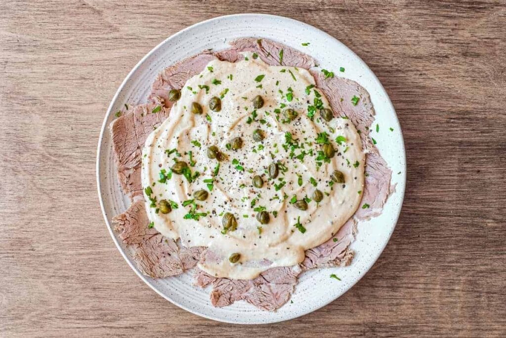 Vitello Tonnato served with tuna cream, peas, and sprinkled herbs, perhaps basil